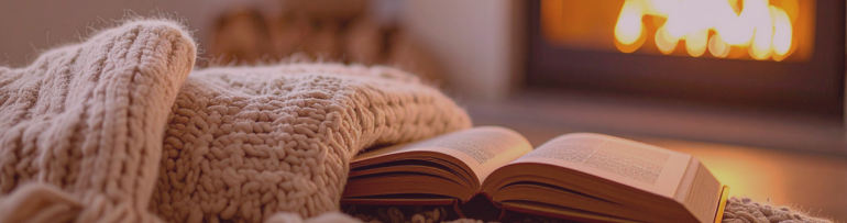 Image of a warm living room, showing an open book in the foreground and an open fire in the background creating wintery appeal
